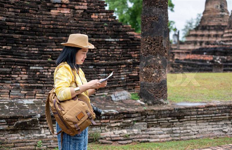 Asian tourist woman see map at ancient of pagoda temple thai architecture at Sukhothai,Thailand. Female traveler in casual thai cloths style visiting city concept, stock photo