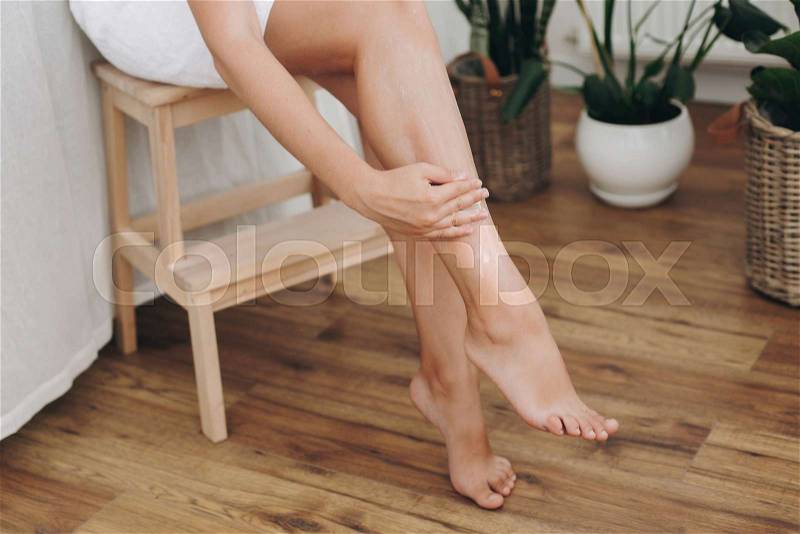 Skin care and wellness concept. Girl hand with moisturizer cream smearing legs for soft skin result. Young woman applying cream on her legs after shaving in bathroom ..., stock photo