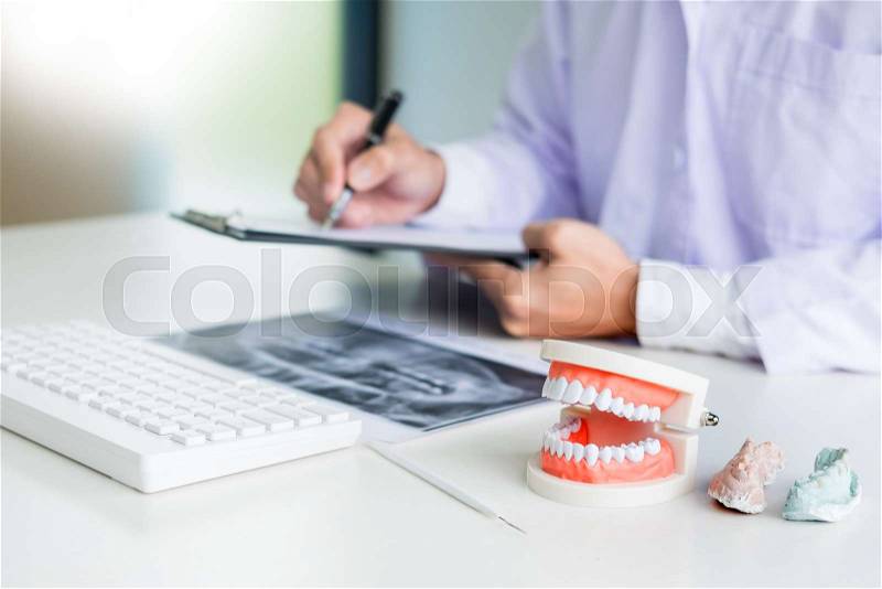 Concentrated dentist sitting at table with jaw samples tooth model in dental office professional dental clinic, stock photo