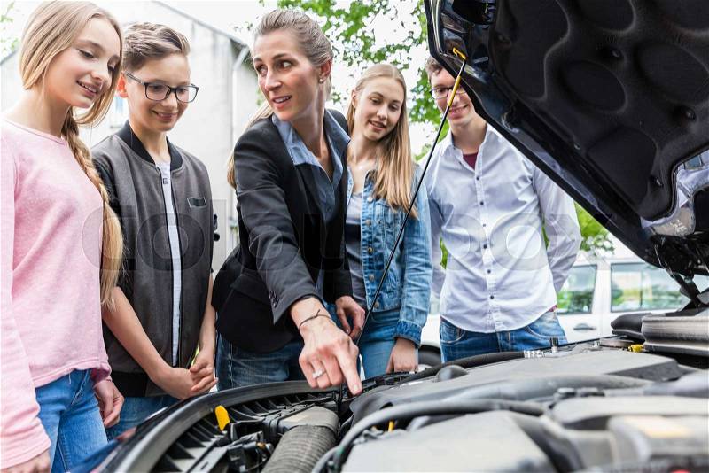Driving teacher showing class the engine of car, letting them look under the hood, stock photo