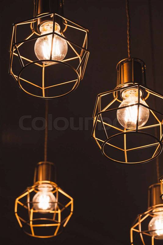 Ceiling chandelier with hanging bulb lamps, yellow LED lighting elements with metal wire frame lampshades, vertical photo with selective focus, stock photo