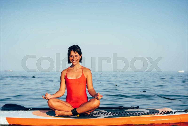 Young woman doing yoga on sup board with paddle. Meditative pose, stock photo