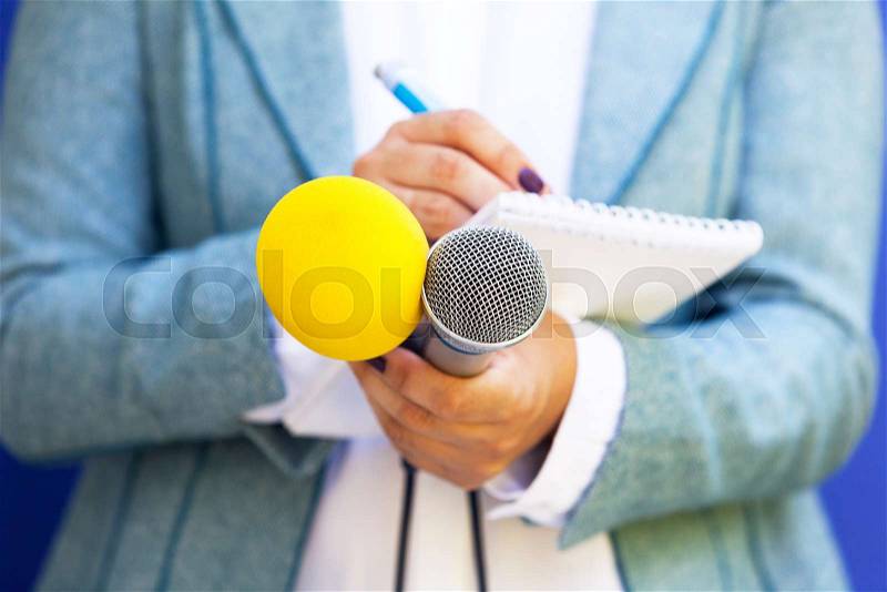 Female journalist at news conference, writing notes, holding microphone, stock photo