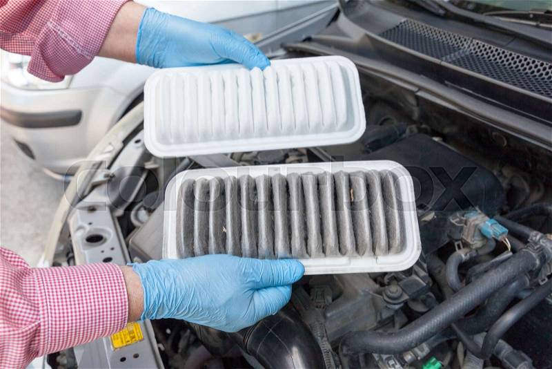 Auto mechanic wearing protective work gloves holding dirty and clean air filters over a car engine. Internal combustion engine air filters, stock photo