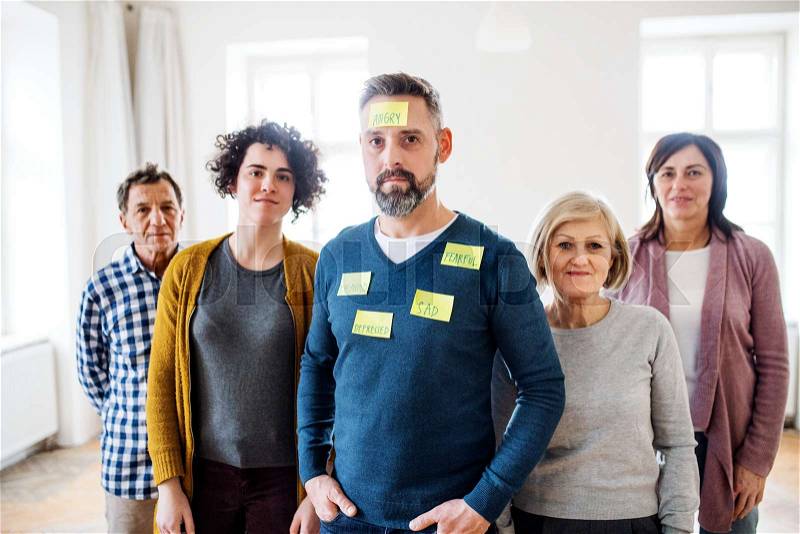 A portrait of young and old people standing with negative emotions adhesive notes during group therapy, stock photo