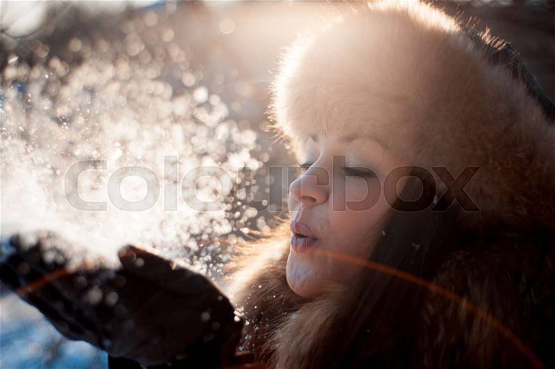 Girl in hat with ear flaps blowing on the snow, stock photo