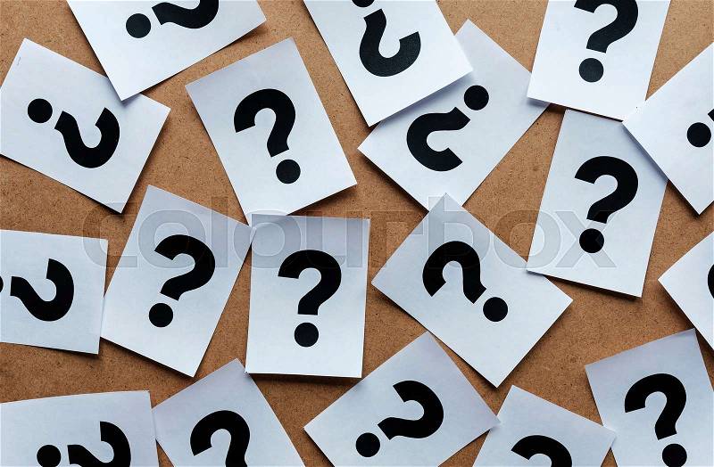 Question marks on paper cards scattered randomly over a wooden background in a conceptual image, stock photo