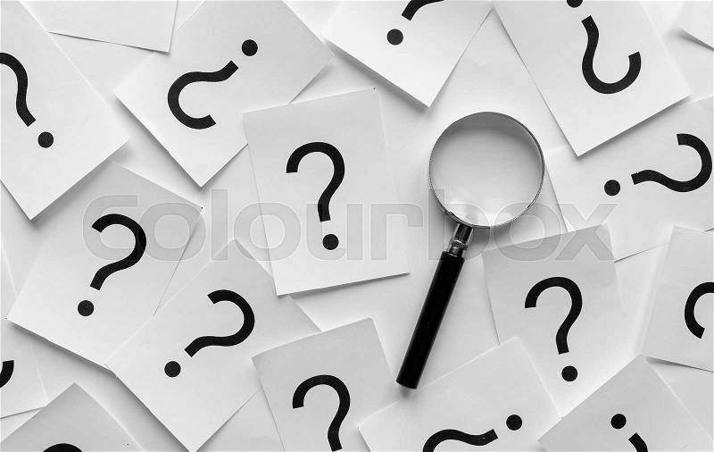 Background pattern of random question marks printed on white cards with a magnifying glass overlying them, stock photo