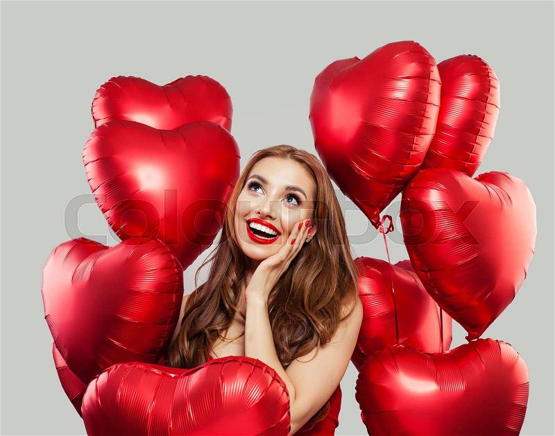 Excited woman with red heart balloons on white background. Happy surprised model girl with red lips makeup, long curly hair. Gift, sale and Valentine\'s day concept, stock photo