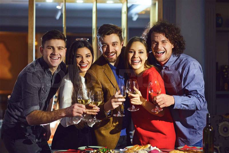 Friends in a restaurant with glasses of wine are smiling at a meeting in the evening, stock photo