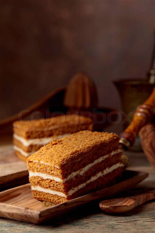 Homemade layered honey cake with cream on a old wooden table, stock photo