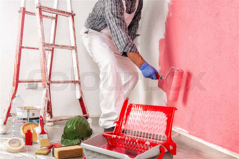 Caucasian house painter worker in white work overalls, with the roller painting the wall with colorful painting. Construction industry, stock photo