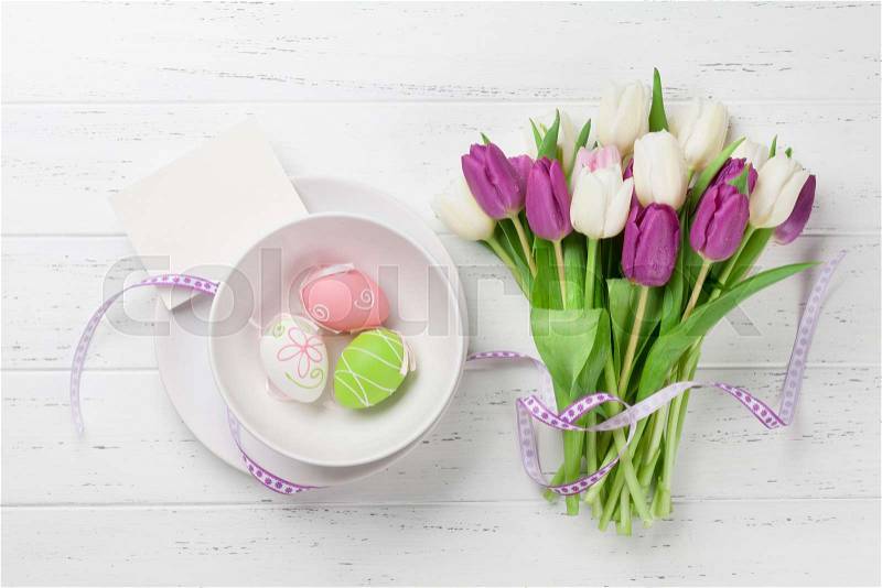 Easter greeting card with tulip flowers bouquet and easter eggs. Top view over white wooden table with space for your greetings, stock photo