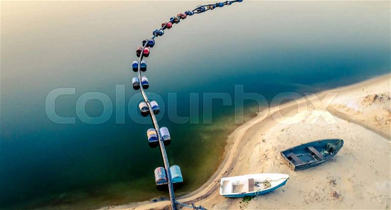 Aerial view of blue tube with barrels on the lake and two boates on sandy beach, stock photo