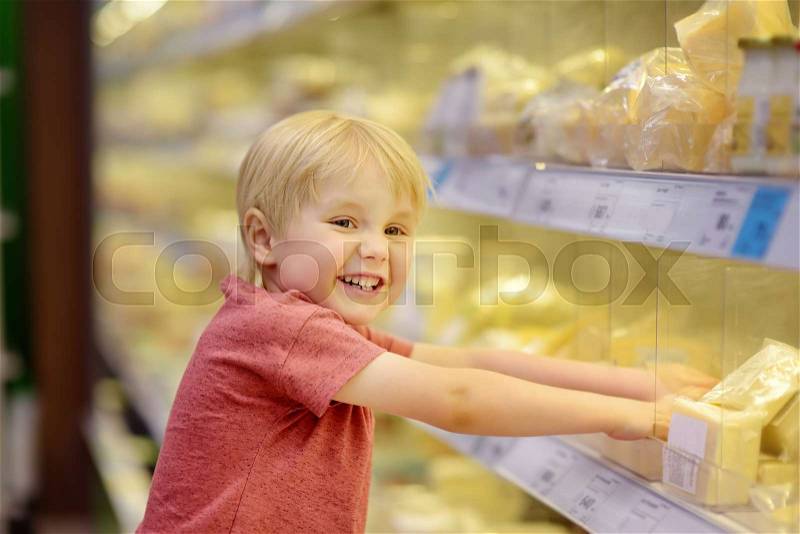 Cute little boy in a food store or a supermarket choosing cheese and butter, fresh dairy. Healthy lifestyle for young family with kids, stock photo