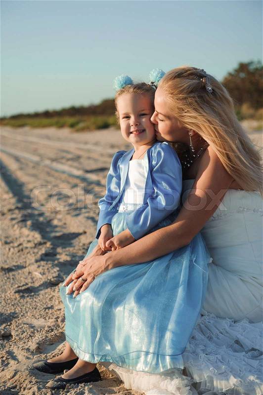 Happy mother in the wedding dress with her daughter on the beach, stock photo