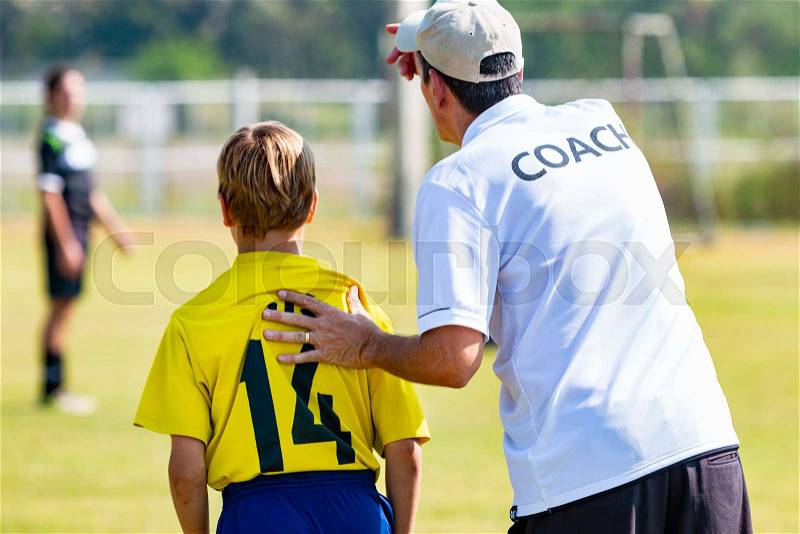 Back view of male football coach in white COACH shirt at an outdoor sport field sending his young boy player in the game, good for coaching or football concept, stock photo
