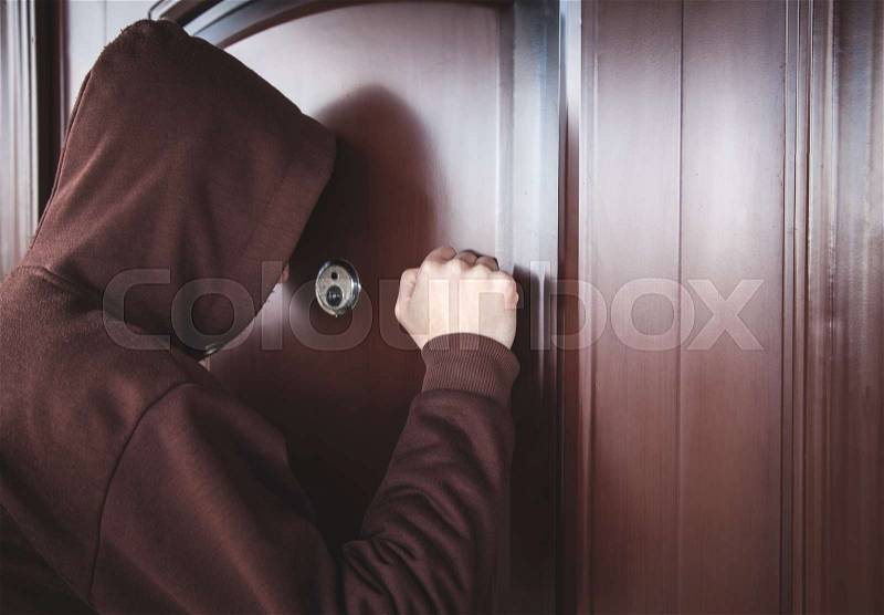 Hooded man knocking on door, stock photo