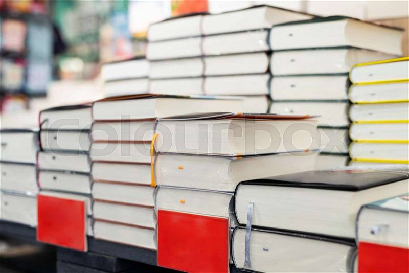 Bookstore shelf with pile of new books with red empty plate. New arrivals at bookshop. Presentation of book. Copyspace, stock photo