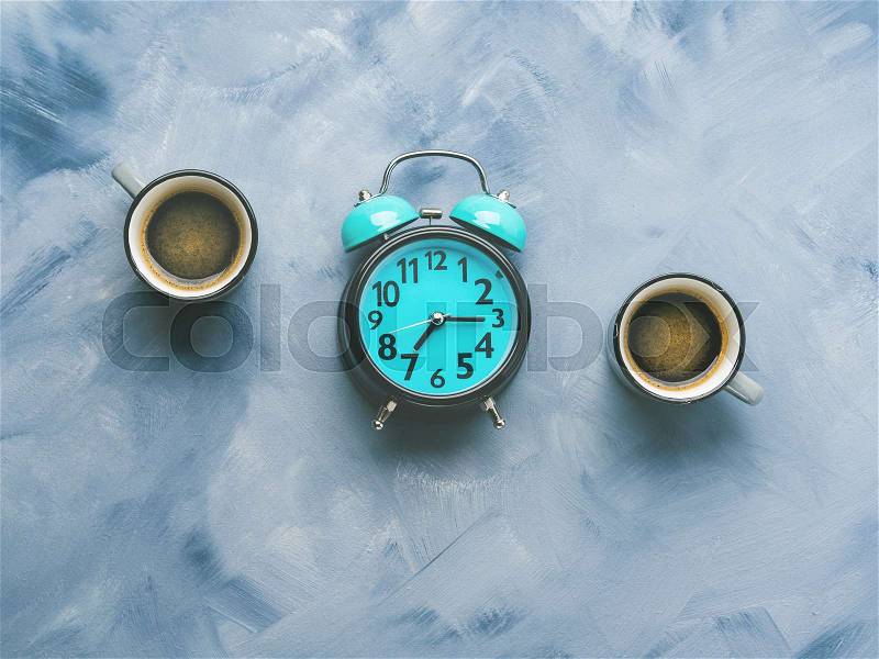 Two coffee cups and alarm clock on sky blue painted background. Minimal flat lay, stock photo