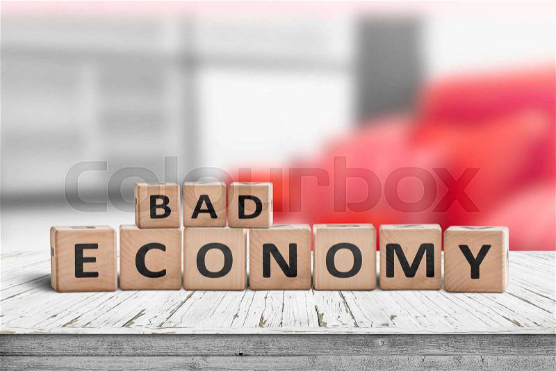 Bad economy sign on a wooden desk in an office with red color in the background, stock photo