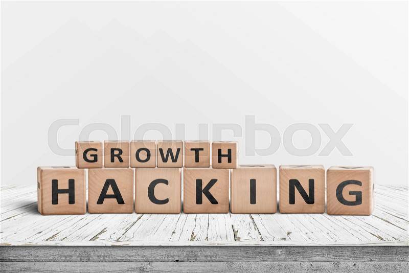 Growth hacking sign on a wooden desk with a grey wall in the background, stock photo