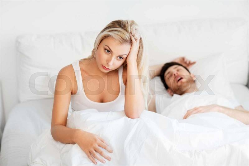 Sleeping problems and people concept - unhappy woman lying in bed with snoring man, stock photo