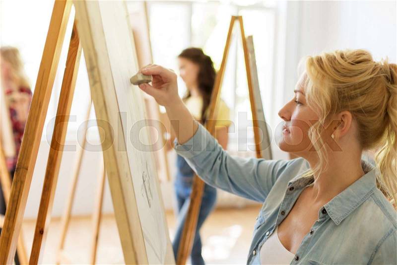Art school, creativity and people concept - woman with eraser and easel drawing at studio, stock photo