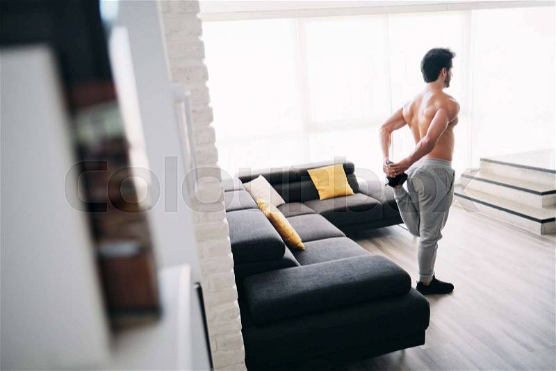 Bare chested young man stretching muscles before starting a workout routine. Handsome hispanic male athlete exercising for wellness in his living room. Latino people ..., stock photo