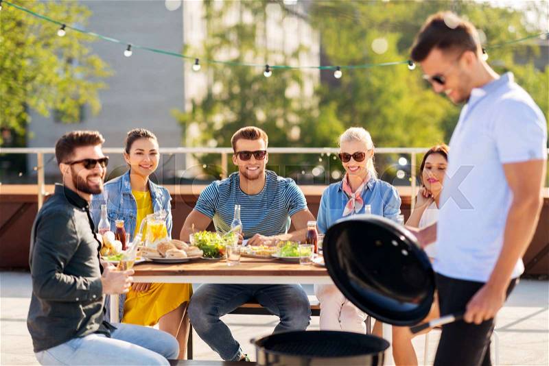 Leisure and people concept - happy man grilling on bbq and friends at rooftop party, stock photo