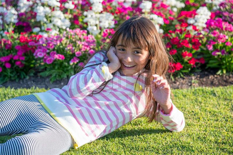 Happy young girl enjoying outdoor life lying down on a beautiful garden, stock photo