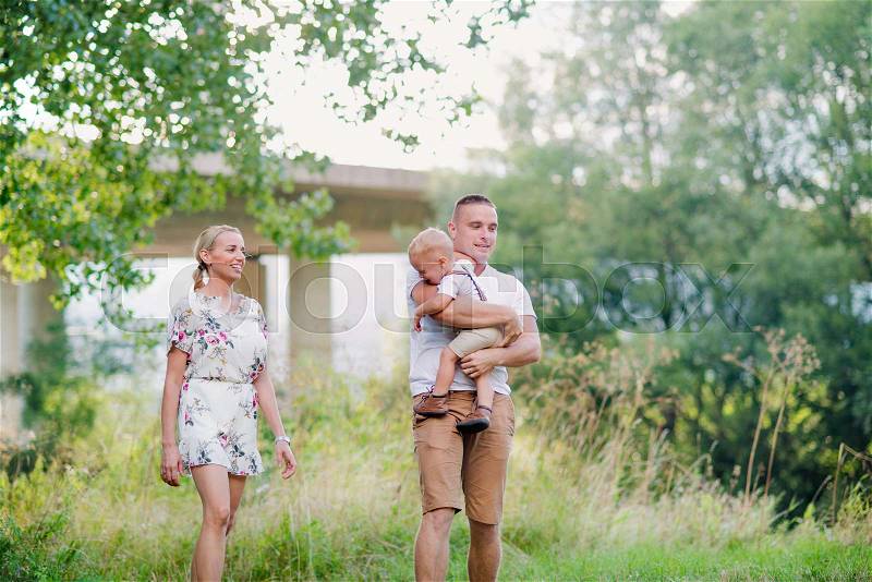 A young family with a small crying toddler boy walking in sunny summer nature, stock photo