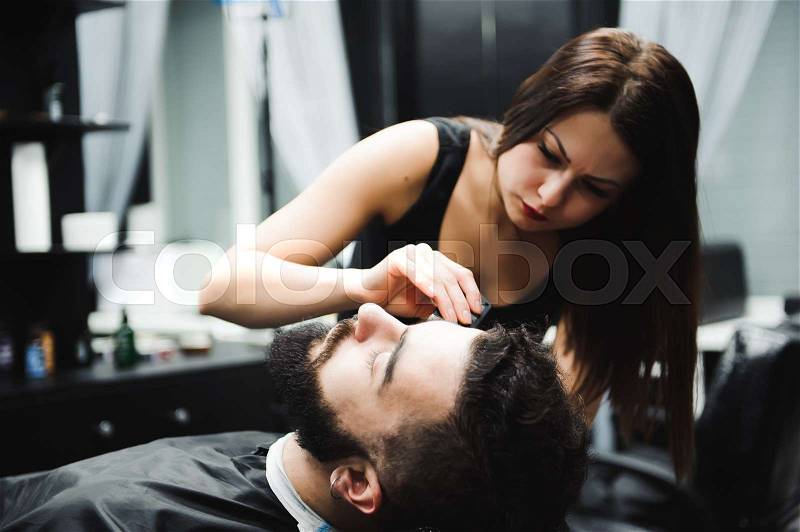 Master cuts hair and beard of men in the barbershop, hairdresser makes hairstyle for a young man, stock photo