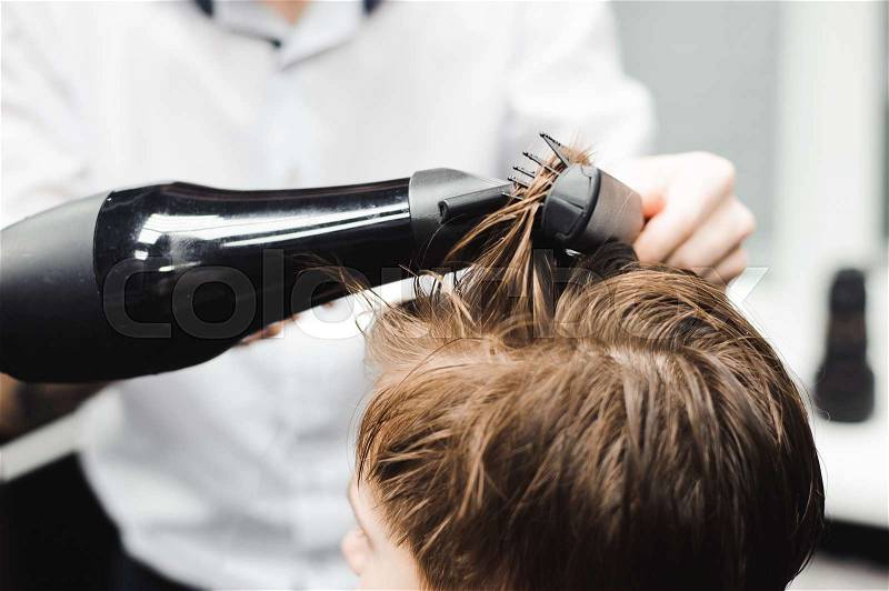 Master cuts hair of a boy in the barbershop, hairdresser makes hairstyle for a boy, stock photo