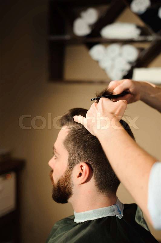 Master cuts hair and beard of men in the barbershop, hairdresser makes hairstyle for a young man, stock photo
