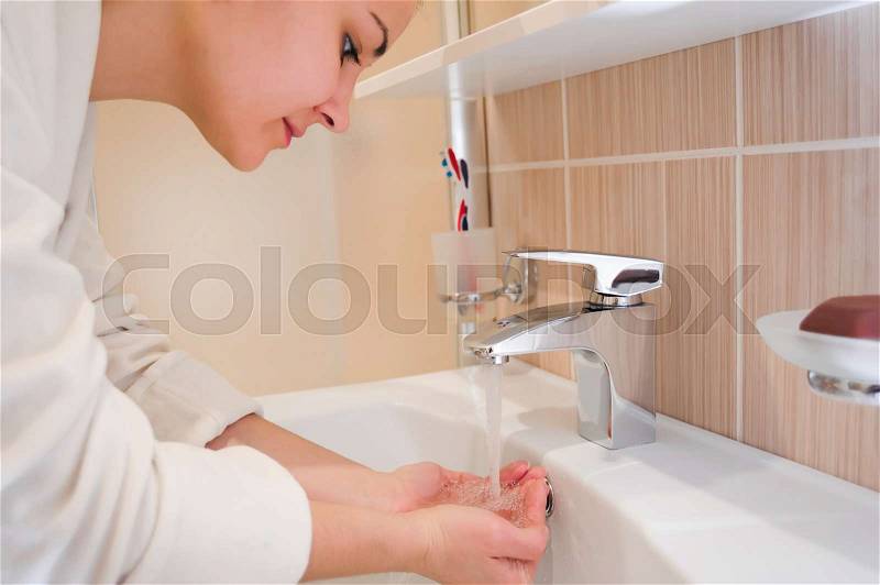 Young female washing her face in a bathroom, stock photo