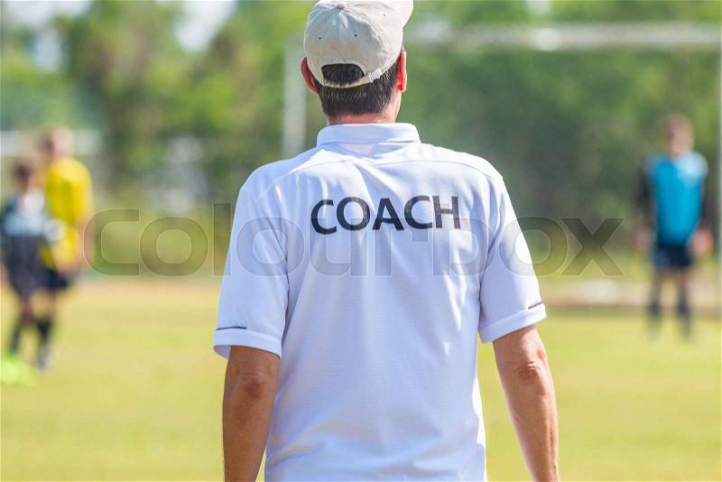 Back of male football coach wearing white COACH shirt at an outdoor sport field coaching his team during a game, good for sport or coaching concept, stock photo