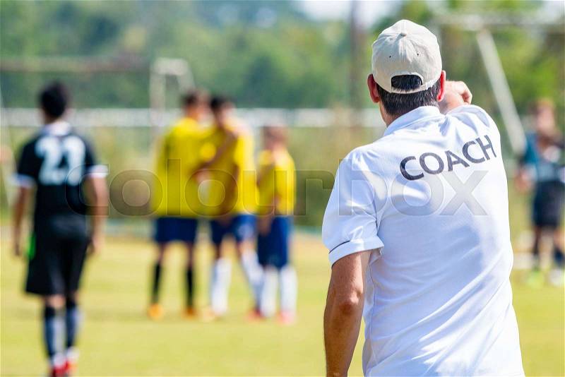 Back of male football coach wearing white COACH shirt at an outdoor sport field coaching his team during a game, good for sport or coaching concept, stock photo