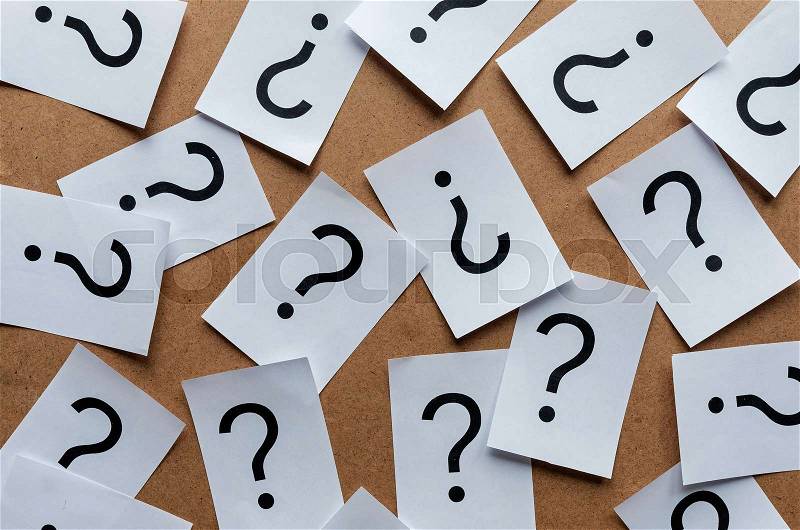 Black question marks on paper cards scattered randomly over a wooden background, stock photo