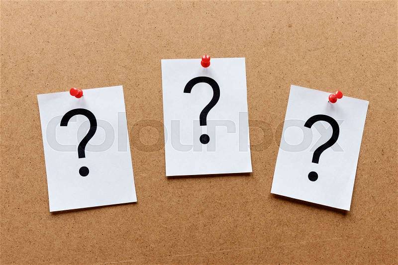 Three question marks pinned in a row with colorful red thumb tacks on a wooden notice board with copy space in a conceptual image, stock photo