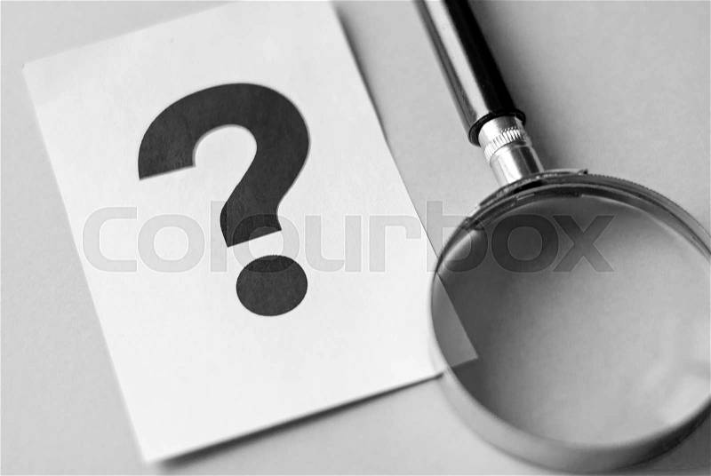 Question mark printed on white sheet of paper and magnifying glass on the table. Search for answers concept with copy space on grey background, stock photo