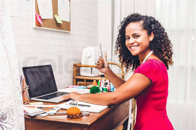 Smiling african american black woman fashion designer working with laptop computer at workshop studio, stock photo