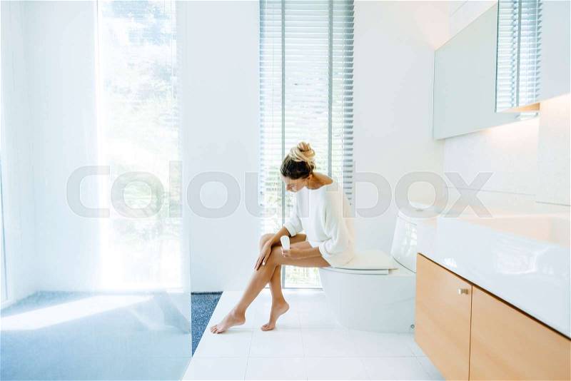 Photo of woman applying body lotion to her legs after shower in luxury bathroom, stock photo