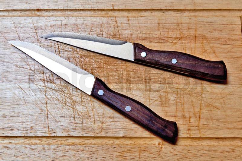 Two steack knifes on textured and scratched wooden plank, view from above with natural light, stock photo