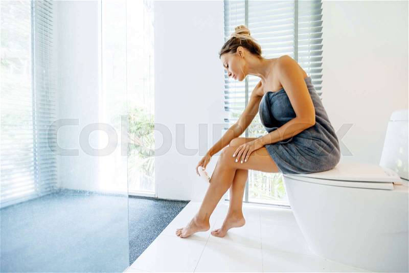 Photo of woman making hair removal on legs with electric epilator. Home depilation after shower in luxury bathroom, stock photo