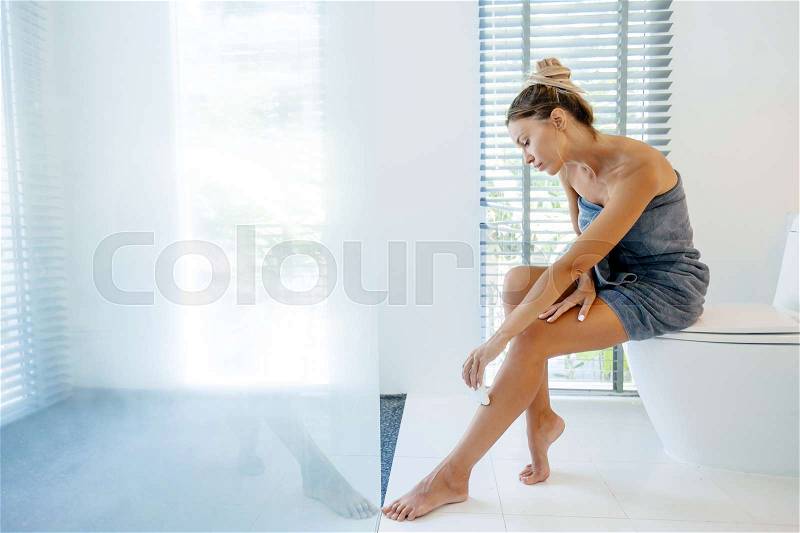 Photo of woman making hair removal on legs with electric epilator. Home depilation after shower in luxury bathroom, stock photo