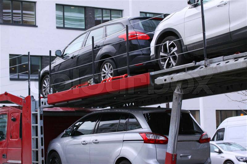 Car shipping auto transport vehicle with cars loaded in front of office buildings, stock photo