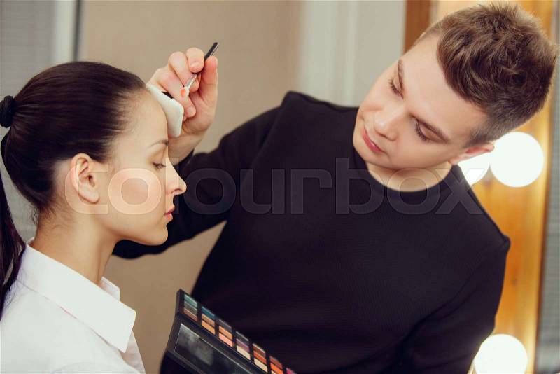Professional makeup artist working with beautiful young woman. The man in female proffesion. Gender equality concept, stock photo