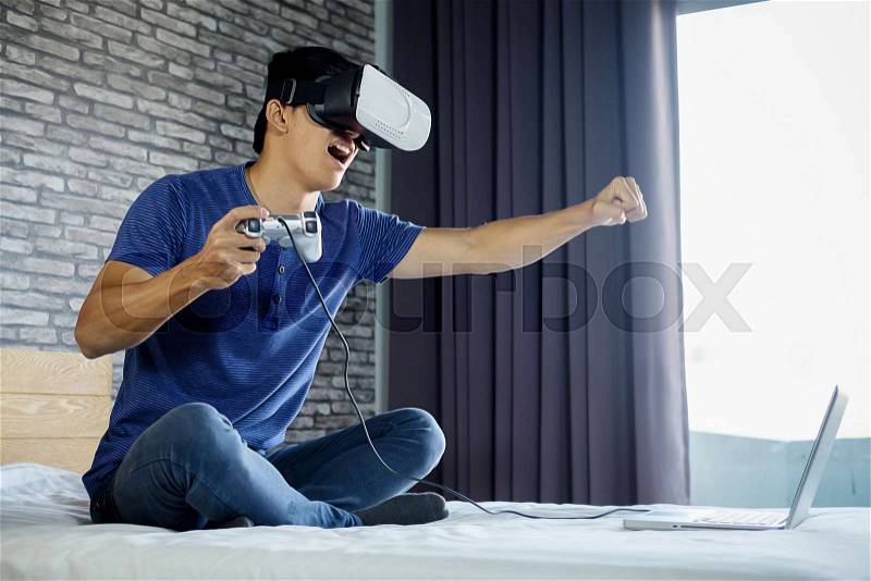 Young man in bedroom playing a virtual reality video game, stock photo