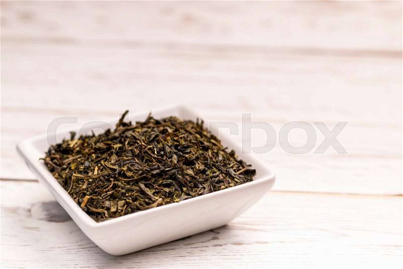 Close-up view of dry moroccan mint tea leaves with in small white ceramic plate on white table, stock photo